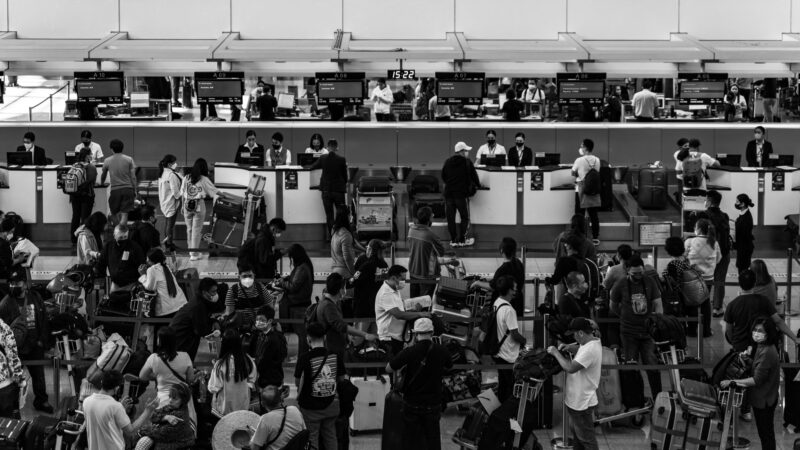 An overshot view of an airport check-in with many people in line carrying luggage.