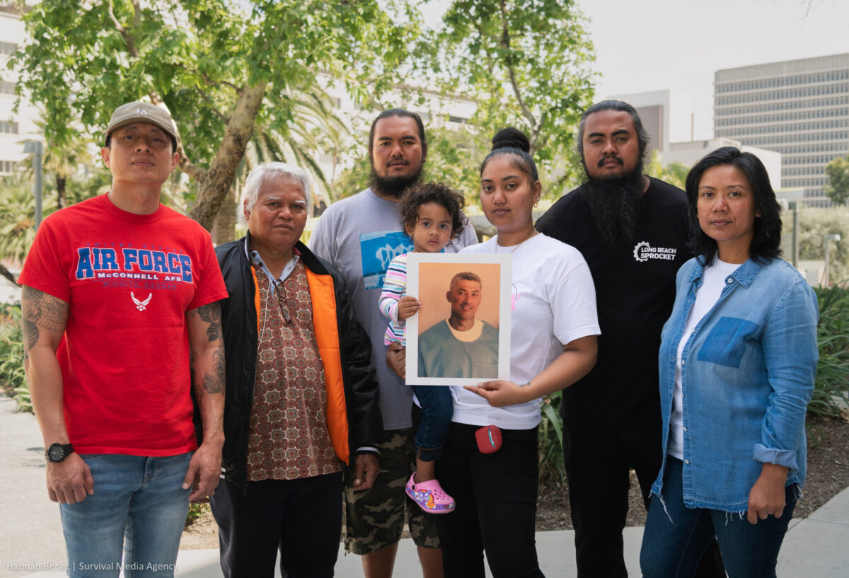 7 of Vithea's family members stand together and hold his photo in his remembrance.