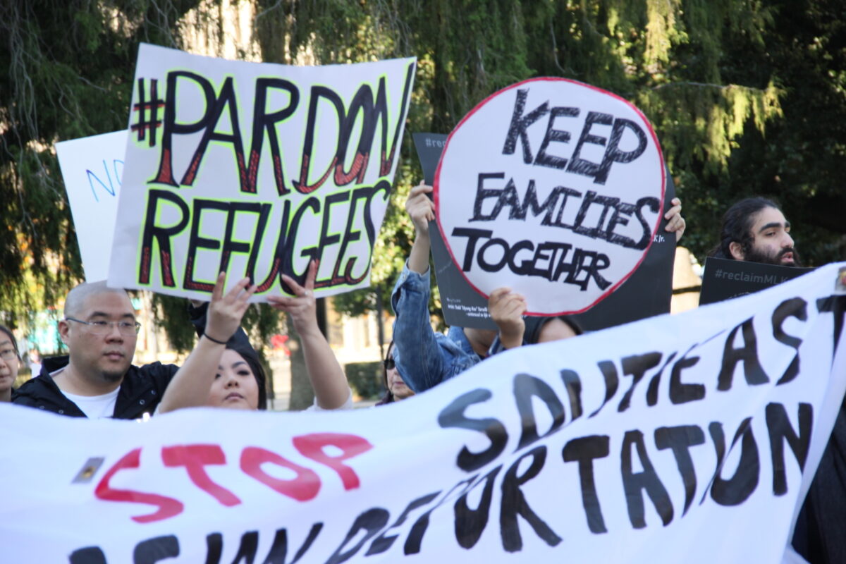 People hold up signs reading "pardon refugees," "keep families together," and "stop southeast asian deportations" in a park