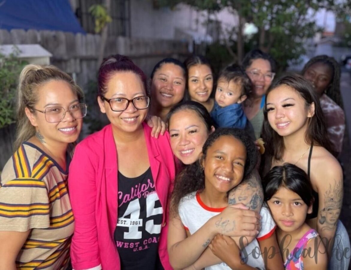 Sophea, wearing a pink blazer, smiles in a group photo with 9 of her close family members and friends.