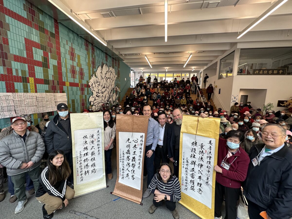 San Francisco Chinatown residents, Community Tenants Association, and staff from the Asian Law Caucus, Legal Assistance to the Elderly, and Ropes & Gray pose together for a photo celebrating the 2022 Valstock settlement. The group stands behind scrolls of Chinese calligraphy honoring the legal team,