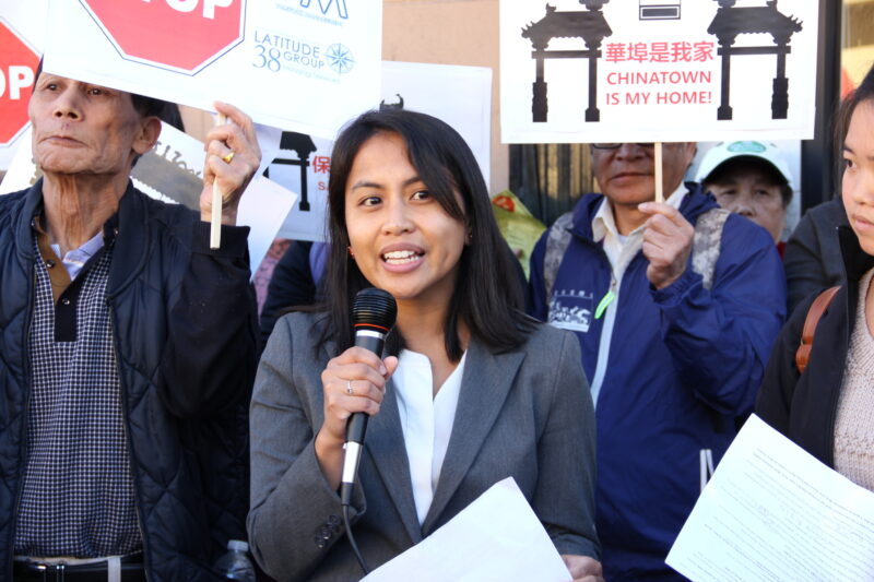 Women with a mic in her hand speaks facing the camera surrounded by people holding signs.