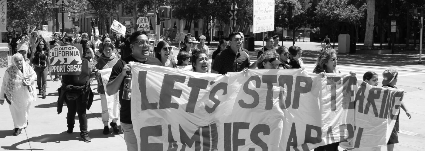 Black and white image of people holding banner reading "let's stop tearing families apart" followed by other protestors