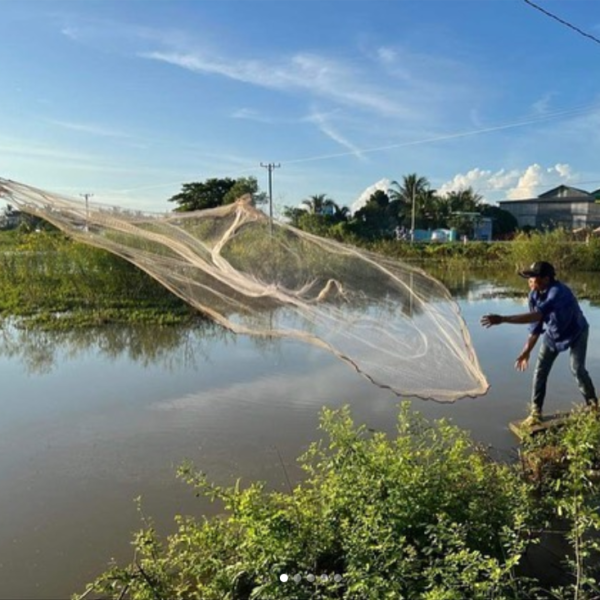 Phoeun throws a fishing net into a lake.