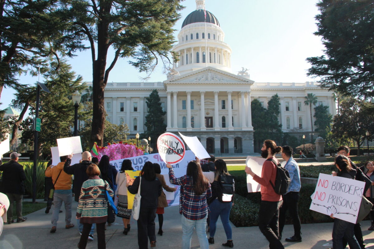 Group of people stand in front of California State Capitol holding protest signs