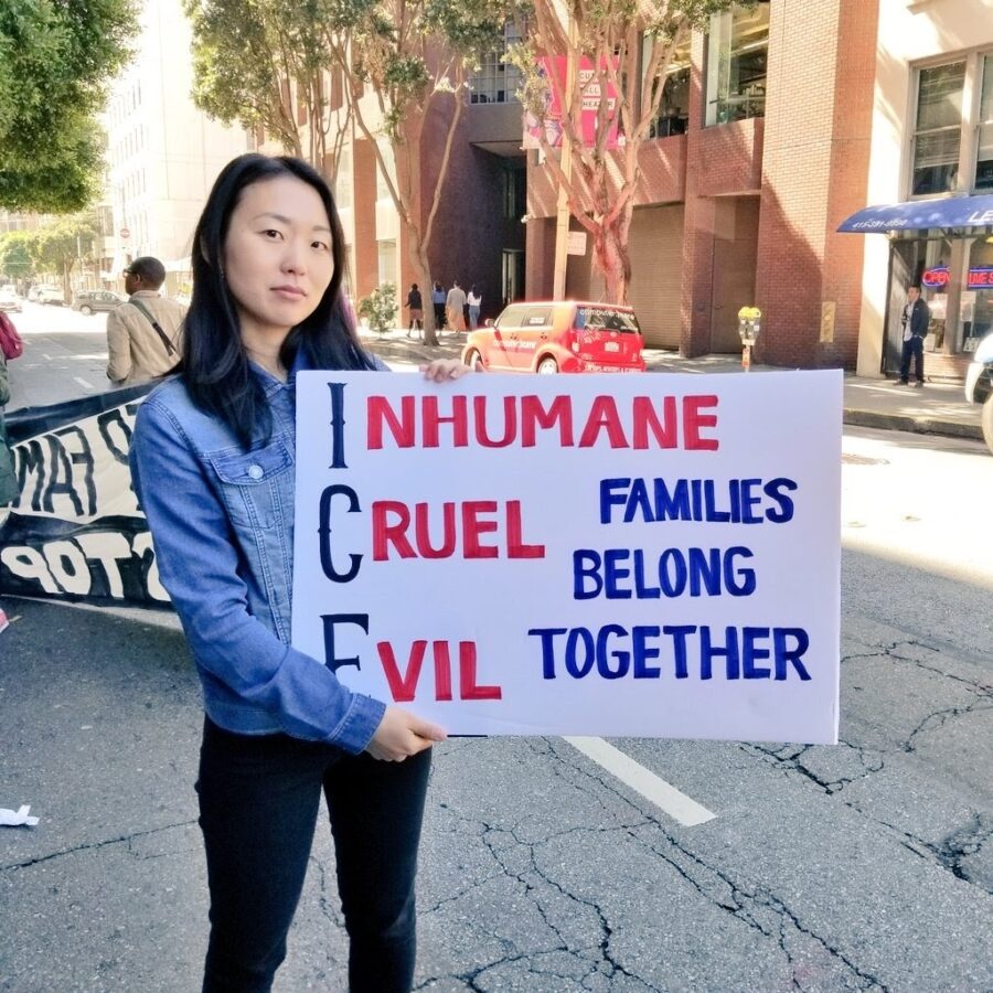 So Young stands on a city street holding a sign that reads "Inhumane Cruel Evil, Families Belong Together"