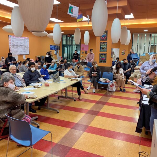 Asian Law Caucus staff member talking on a mic to a room of people sitting at tables at the Chinatown Community Development Center.