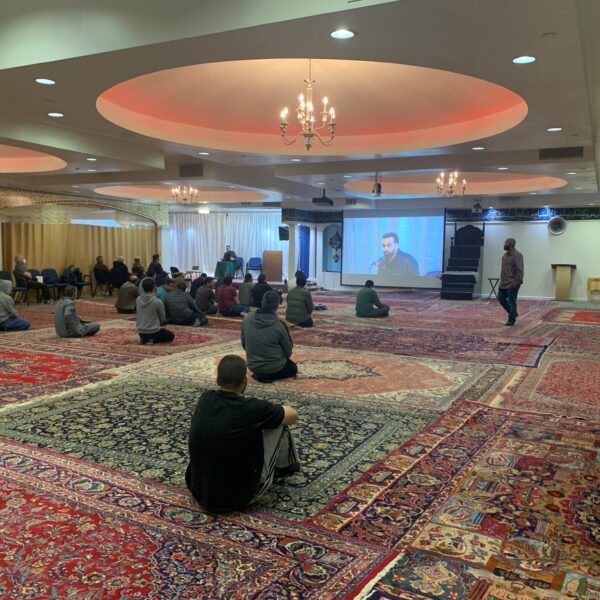 Attendees at the SABA Center are seated on the floor of the mosque listening to a speaker.