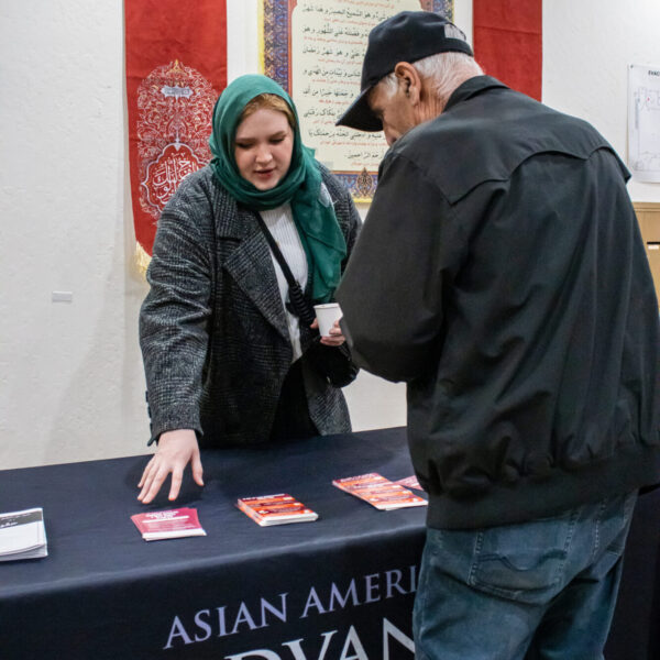 ALC staff member is standing behind the outreach table speaking to a community member about their civil rights and pointing at flyers at SABA Islamic Center. Photo Credit: Jibraan Qureshi