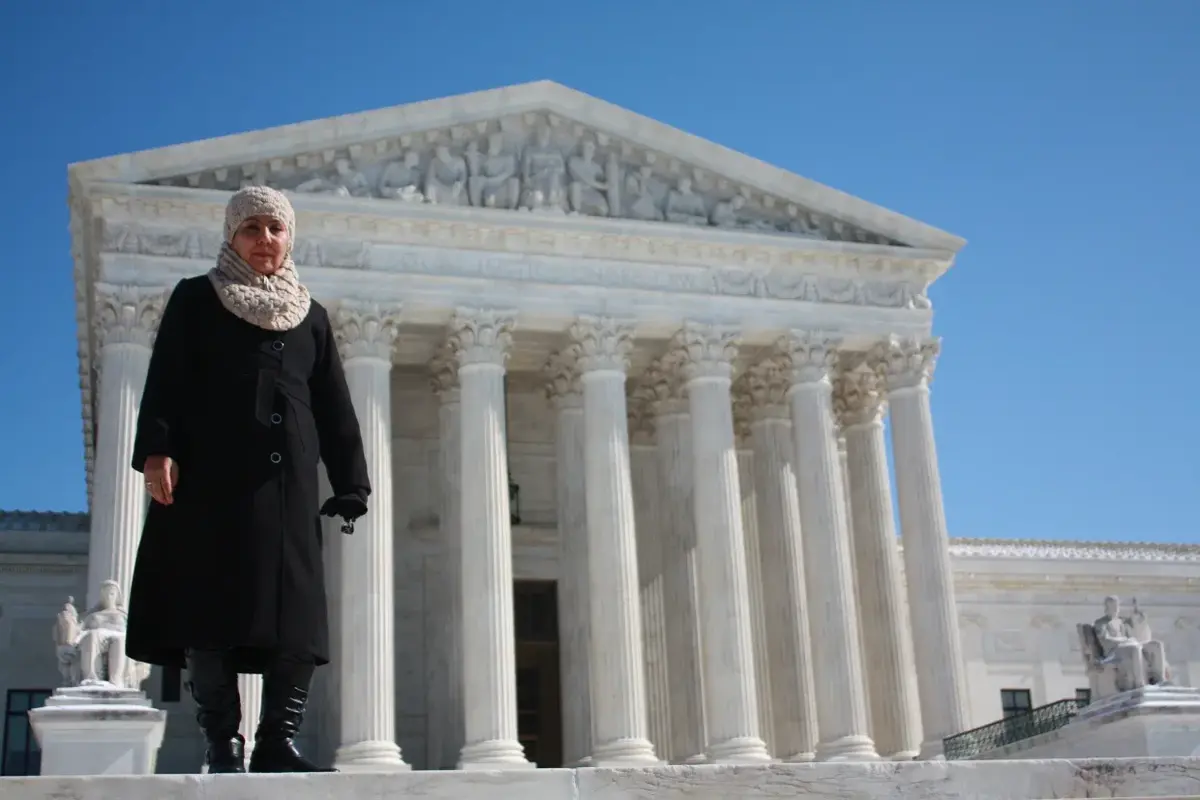 Fauzia Din stands outside the Supreme Court in Washington, D.C., wearing a black coat and woolen scarf and cap.
