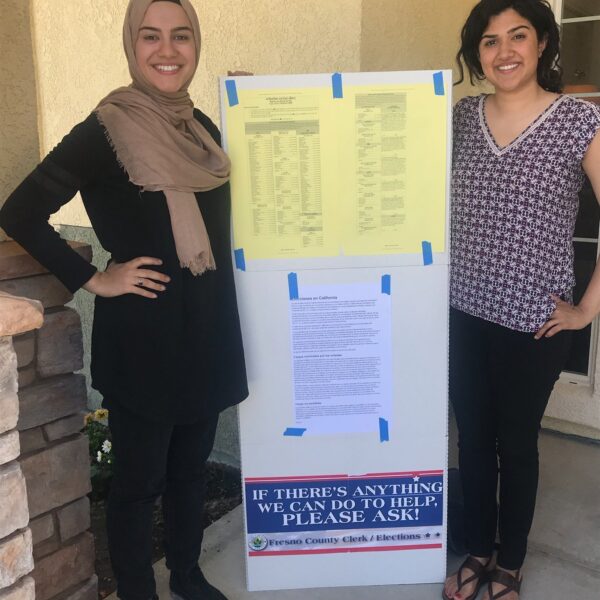 Two women stand with a sign between them at a polling location
