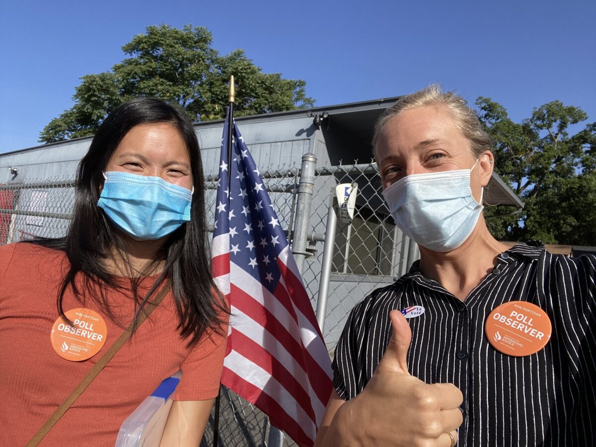 Two California poll monitor volunteers standing side by side. Both are wearing masks and orange stickers that say "Non-Partisan Poll Observer."