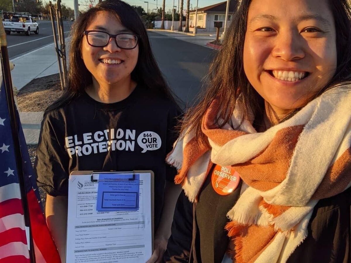 Lauren and her friend joy smile and hold up their 2020 poll monitoring clipboard.