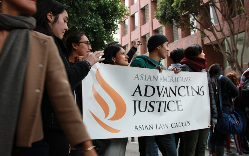 Four people hold a banner with the Asian American Advancing Justice - Asian Law Caucus logo outside at a rally
